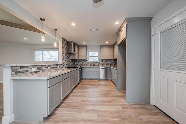 kitchen with stainless steel appliances, visible vents, hanging light fixtures, gray cabinets, and wall chimney exhaust hood