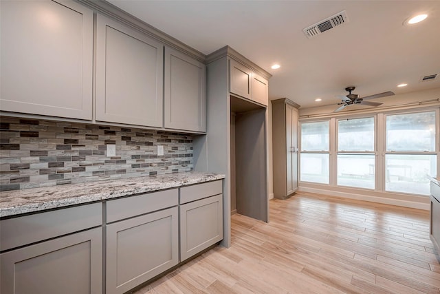 kitchen with light stone counters, gray cabinets, visible vents, backsplash, and light wood-style floors