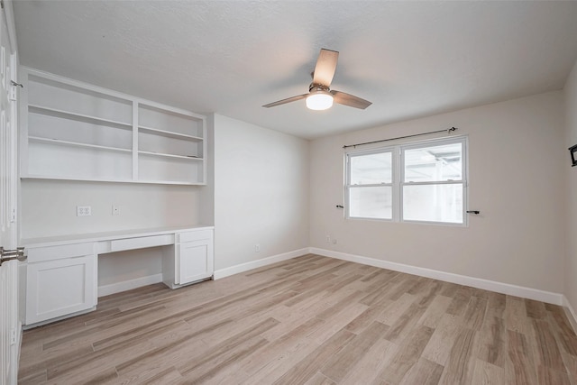 interior space featuring light wood-type flooring, a ceiling fan, baseboards, and built in desk