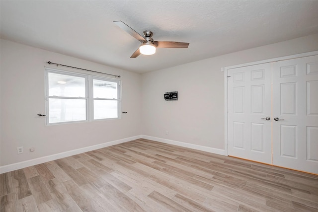 spare room with light wood-style floors, ceiling fan, a textured ceiling, and baseboards