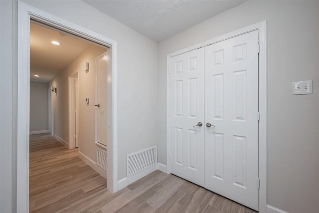 hallway featuring light wood-style floors, baseboards, and visible vents