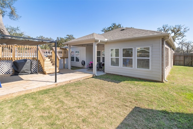 rear view of property featuring fence, a wooden deck, roof with shingles, a lawn, and a patio