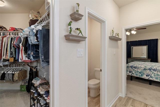 bathroom with wood finished floors, baseboards, ceiling fan, a spacious closet, and toilet