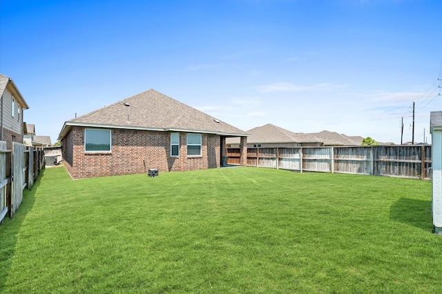 rear view of house featuring brick siding, a yard, a fenced backyard, and roof with shingles