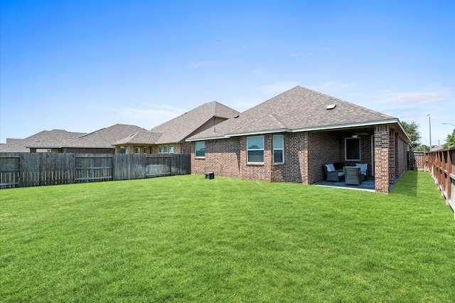 back of house with brick siding, a yard, a shingled roof, a patio area, and a fenced backyard