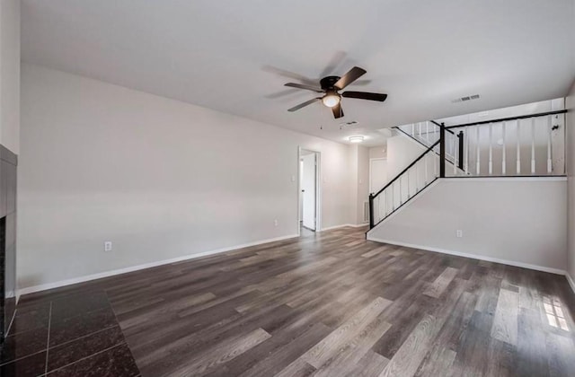 unfurnished living room with dark wood-type flooring, a ceiling fan, visible vents, baseboards, and stairway