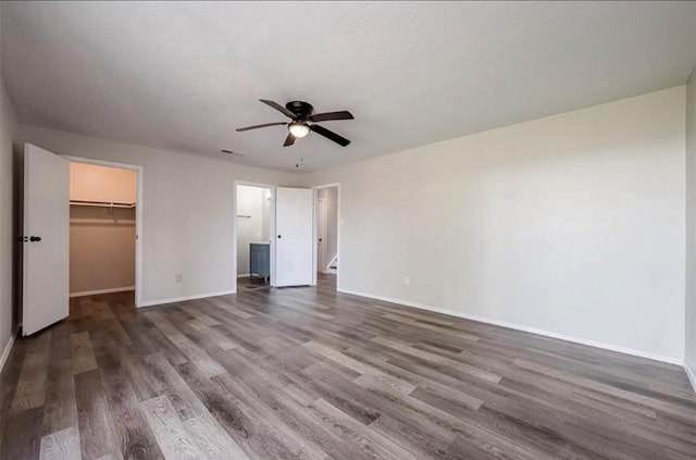 unfurnished bedroom featuring dark wood-style floors, visible vents, a spacious closet, and baseboards