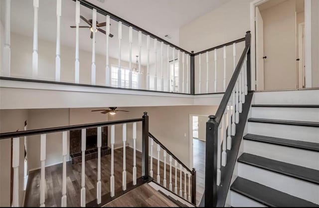 stairs with a towering ceiling, a ceiling fan, and wood finished floors