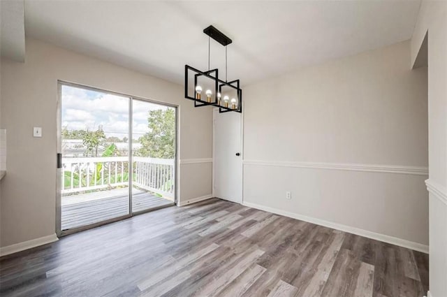 unfurnished dining area featuring an inviting chandelier, wood finished floors, and baseboards