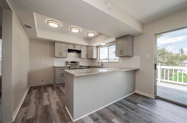 kitchen featuring stainless steel electric stove, a raised ceiling, decorative backsplash, a peninsula, and under cabinet range hood