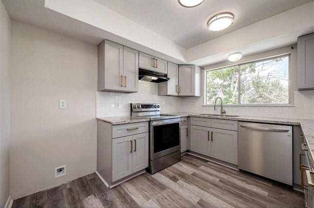 kitchen featuring appliances with stainless steel finishes, a sink, under cabinet range hood, and gray cabinetry