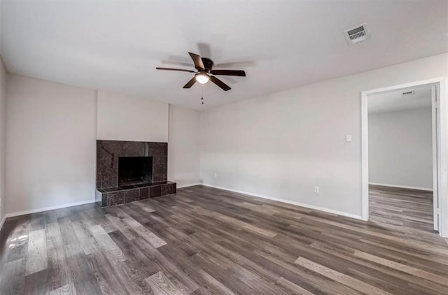 unfurnished living room featuring a tile fireplace, dark wood-style flooring, visible vents, baseboards, and a ceiling fan