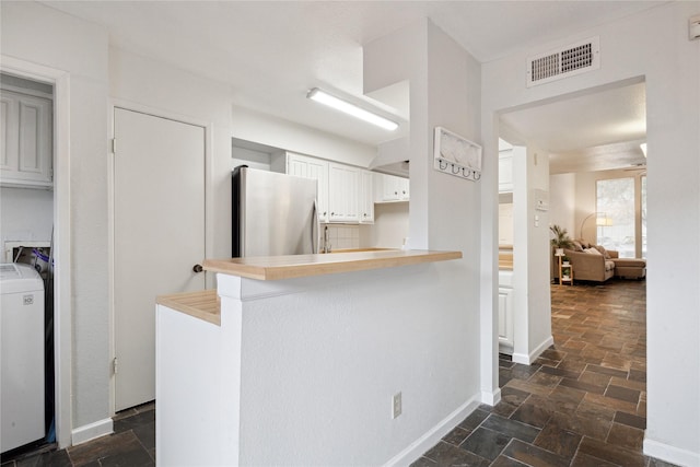 kitchen with washer / clothes dryer, visible vents, freestanding refrigerator, and stone tile flooring