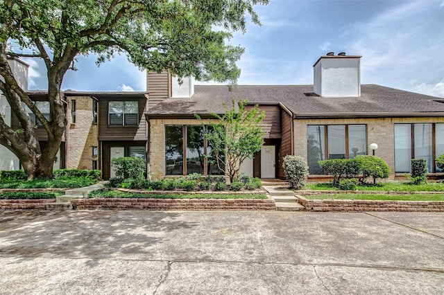 multi unit property with brick siding, a chimney, and a shingled roof