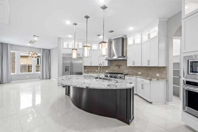 kitchen featuring wall chimney range hood, glass insert cabinets, white cabinets, and built in appliances