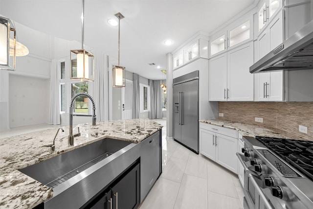 kitchen with pendant lighting, glass insert cabinets, white cabinetry, wall chimney range hood, and high quality appliances