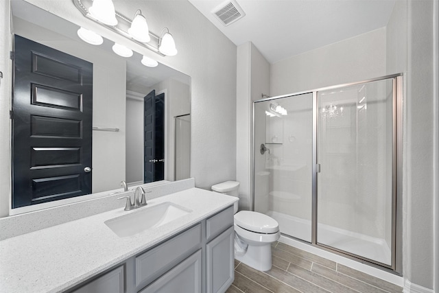 bathroom with visible vents, toilet, vanity, a shower stall, and wood finish floors