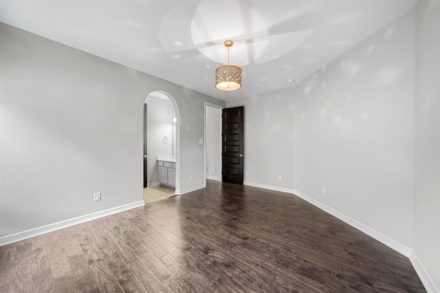 empty room with arched walkways, baseboards, and wood finished floors