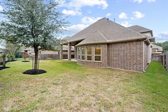 rear view of property featuring a yard, brick siding, roof with shingles, and a fenced backyard