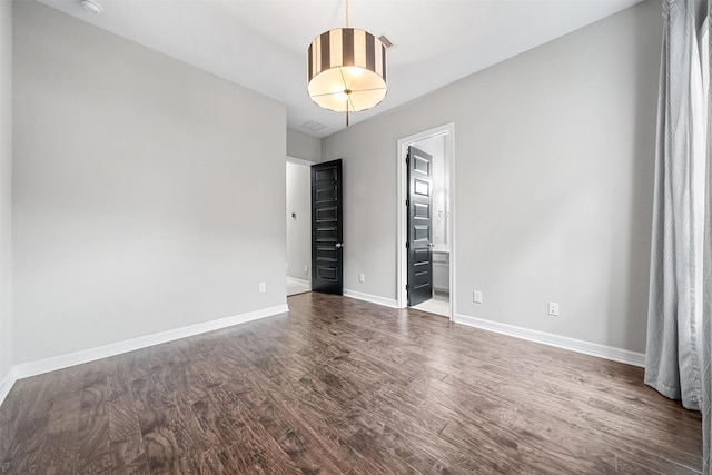 unfurnished bedroom with ensuite bathroom, dark wood finished floors, and baseboards