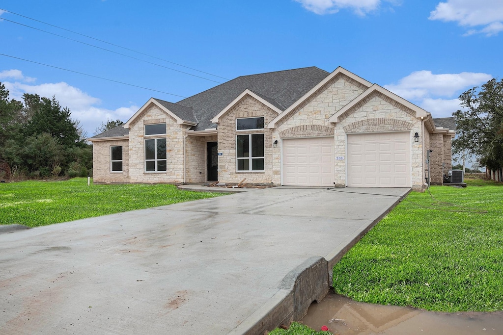 view of front of home with a front lawn, driveway, stone siding, roof with shingles, and a garage