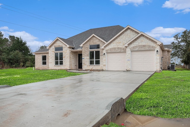 view of front of home with a front lawn, driveway, stone siding, roof with shingles, and a garage