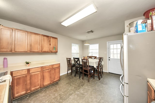 kitchen featuring light countertops, brown cabinetry, freestanding refrigerator, and pendant lighting