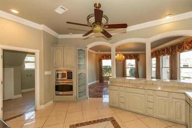 kitchen with light tile patterned floors, cream cabinets, appliances with stainless steel finishes, glass insert cabinets, and plenty of natural light