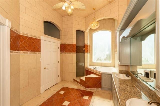 full bathroom with double vanity, tile walls, tile patterned floors, a sink, and a bath