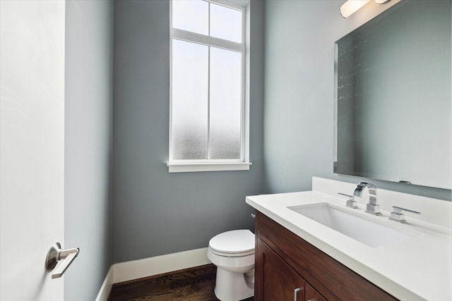 half bath with baseboards, vanity, toilet, and wood finished floors