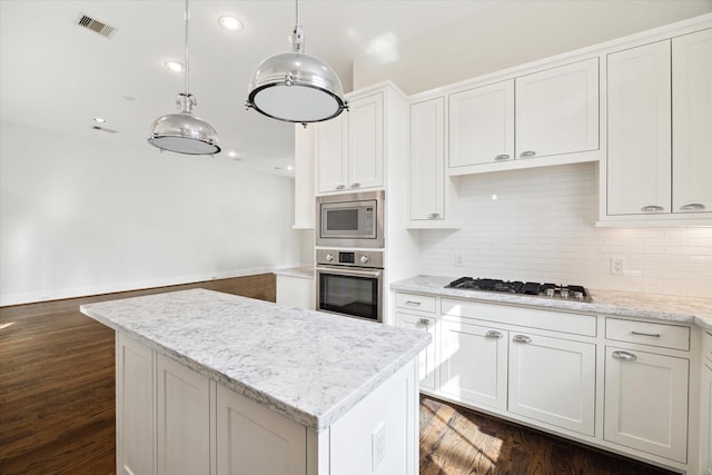 kitchen featuring hanging light fixtures, appliances with stainless steel finishes, white cabinets, a kitchen island, and light stone countertops