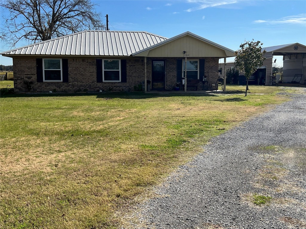 single story home featuring gravel driveway, brick siding, metal roof, and a front lawn