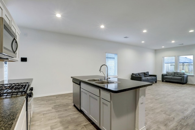 kitchen featuring a sink, open floor plan, appliances with stainless steel finishes, light wood-type flooring, and an island with sink