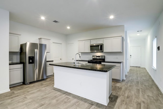 kitchen with appliances with stainless steel finishes, an island with sink, a sink, and light wood-style flooring