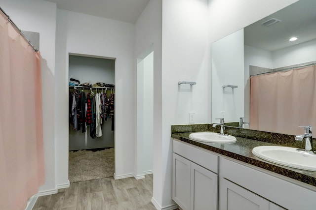 bathroom with a spacious closet, wood finished floors, a sink, and visible vents