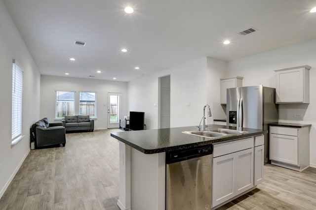 kitchen with stainless steel appliances, dark countertops, open floor plan, white cabinetry, and an island with sink