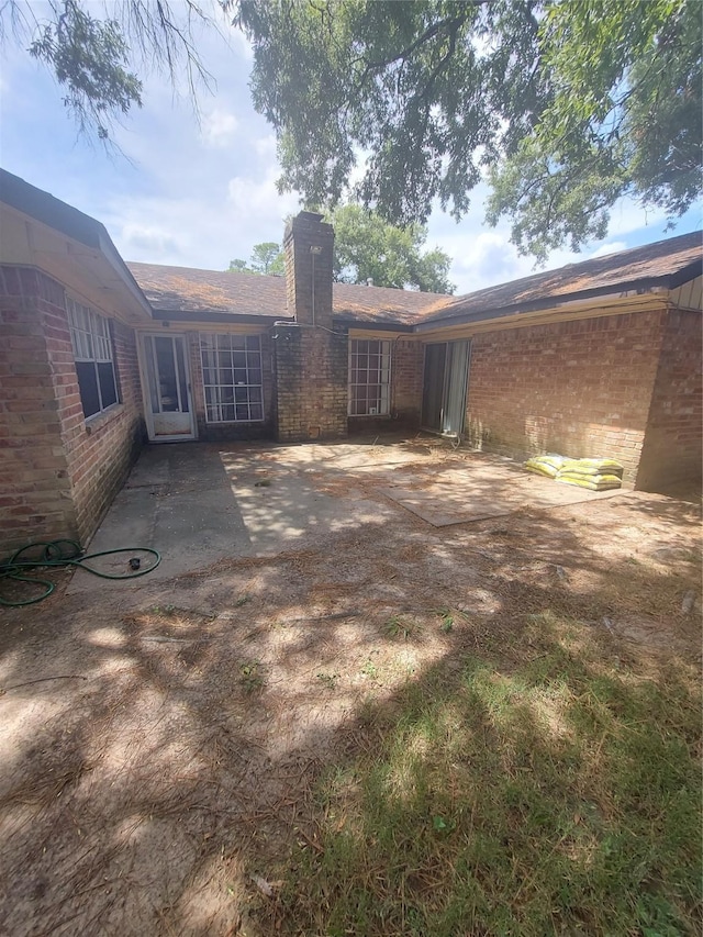 rear view of house featuring a patio, brick siding, and a chimney