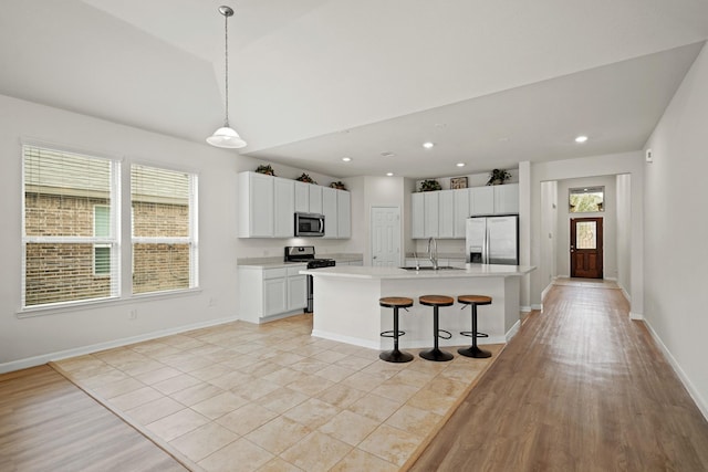 kitchen featuring stainless steel appliances, light countertops, hanging light fixtures, a kitchen island with sink, and white cabinetry