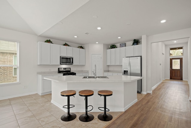 kitchen with light countertops, appliances with stainless steel finishes, a sink, and a center island with sink