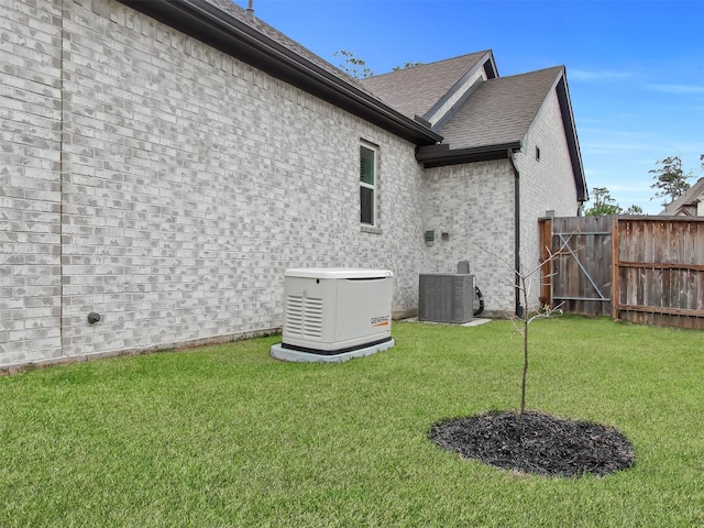 rear view of house featuring central AC unit, brick siding, fence, a yard, and roof with shingles