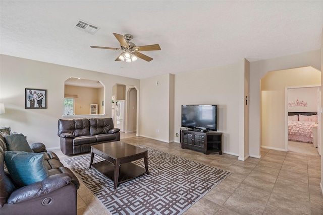 living room featuring arched walkways, light tile patterned floors, visible vents, a ceiling fan, and baseboards