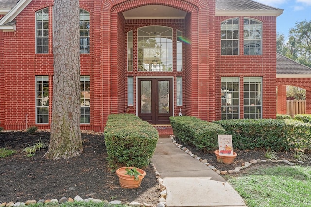 entrance to property with brick siding, roof with shingles, and french doors