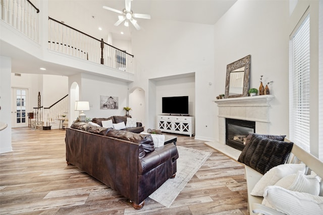 living room with a ceiling fan, light wood finished floors, arched walkways, stairs, and a glass covered fireplace