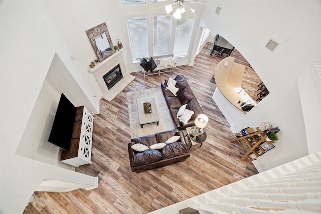 living area featuring visible vents, a premium fireplace, a high ceiling, wood finished floors, and a ceiling fan