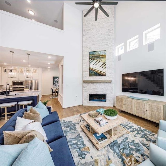 living room featuring ceiling fan with notable chandelier, a stone fireplace, light wood-type flooring, and recessed lighting