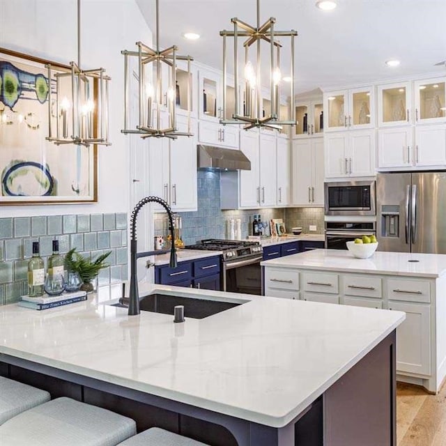 kitchen with under cabinet range hood, appliances with stainless steel finishes, a spacious island, and pendant lighting