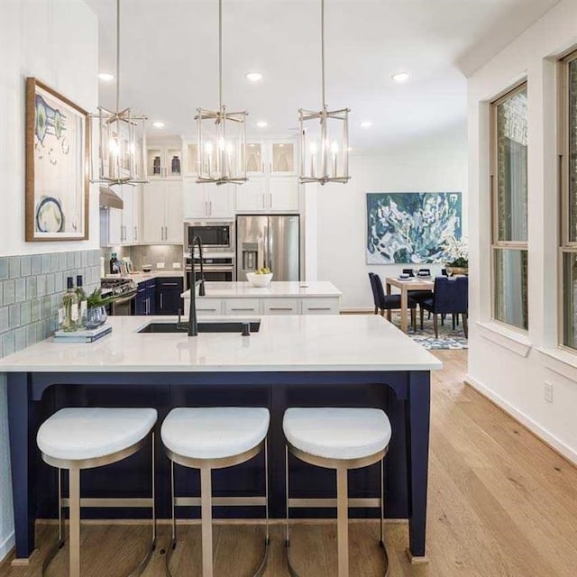 kitchen featuring pendant lighting, stainless steel appliances, light countertops, glass insert cabinets, and white cabinets