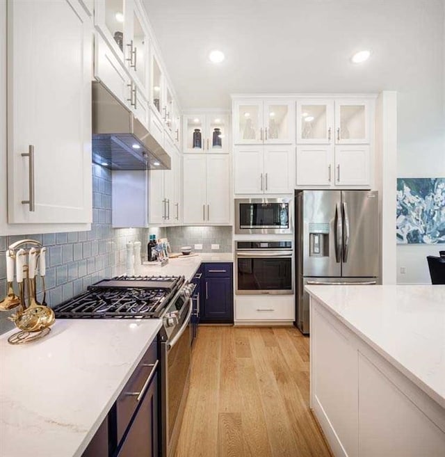 kitchen with under cabinet range hood, appliances with stainless steel finishes, glass insert cabinets, and white cabinets