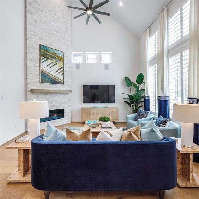 living area featuring baseboards, ceiling fan, wood finished floors, a fireplace, and high vaulted ceiling