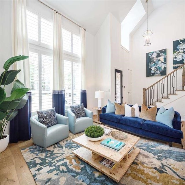 living area with stairs, wood finished floors, a towering ceiling, and an inviting chandelier